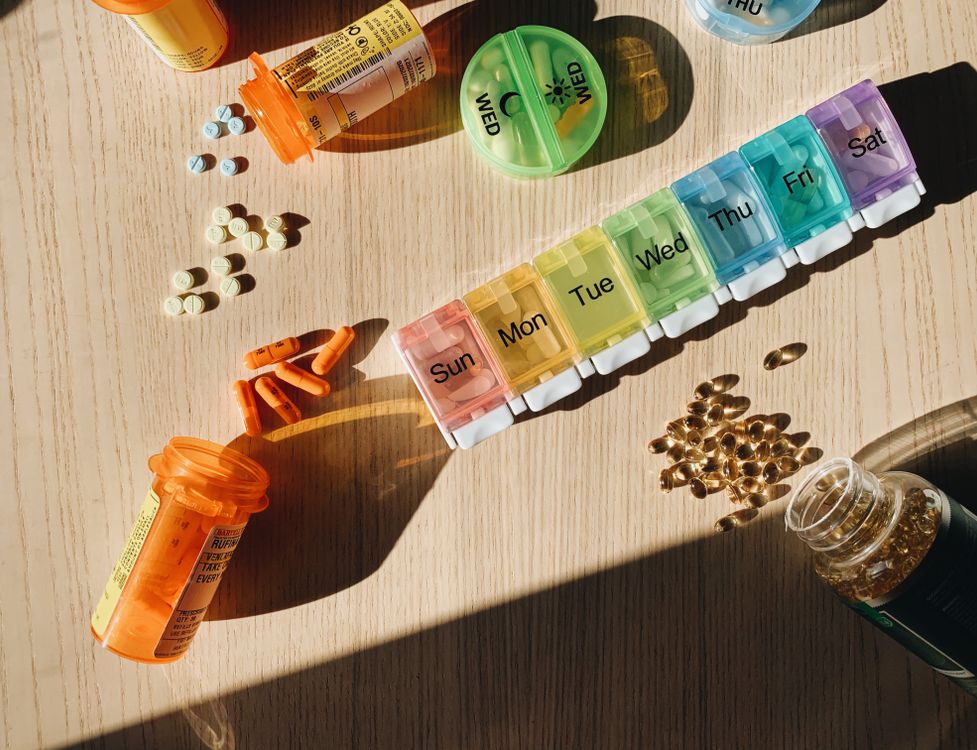 Prescription bottles, tablets, supplement softgels and colorful pill organizers on a sunlit wooden table