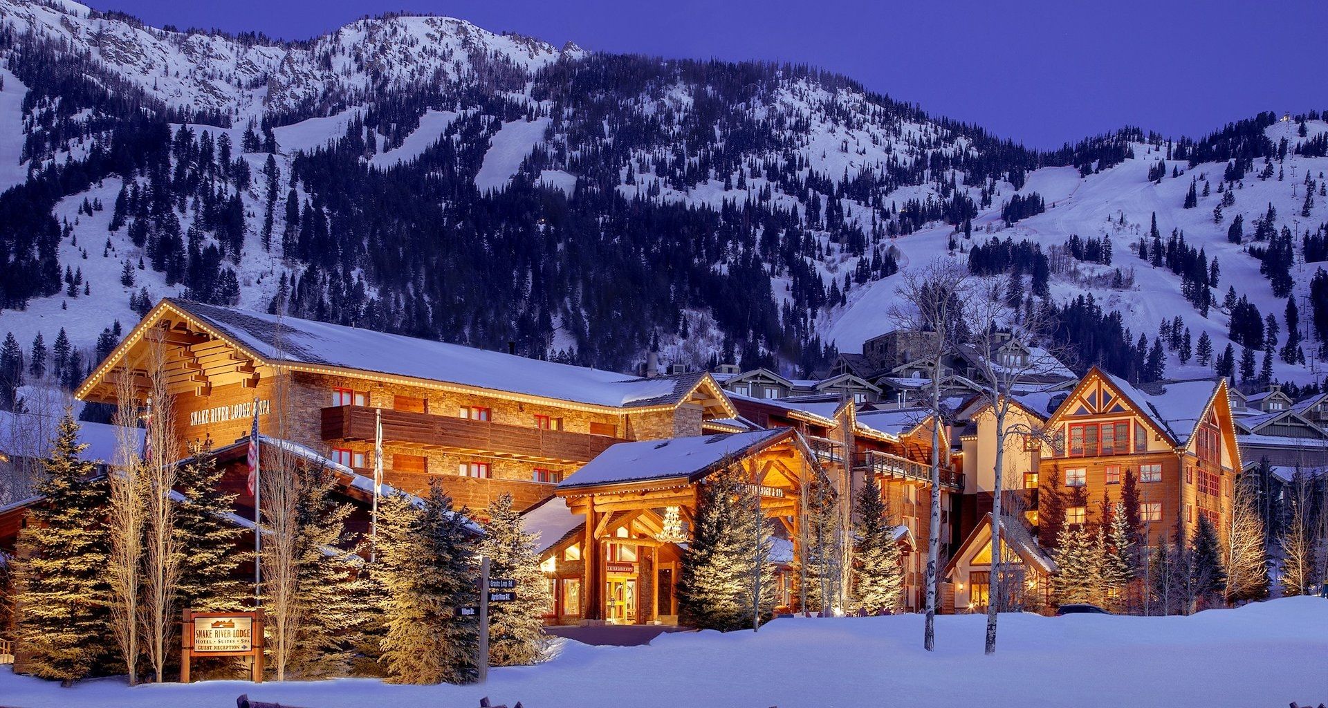Snake River Lodge & Spa exterior at night, alpine lodge glowing warmly against snowy mountain backdrop