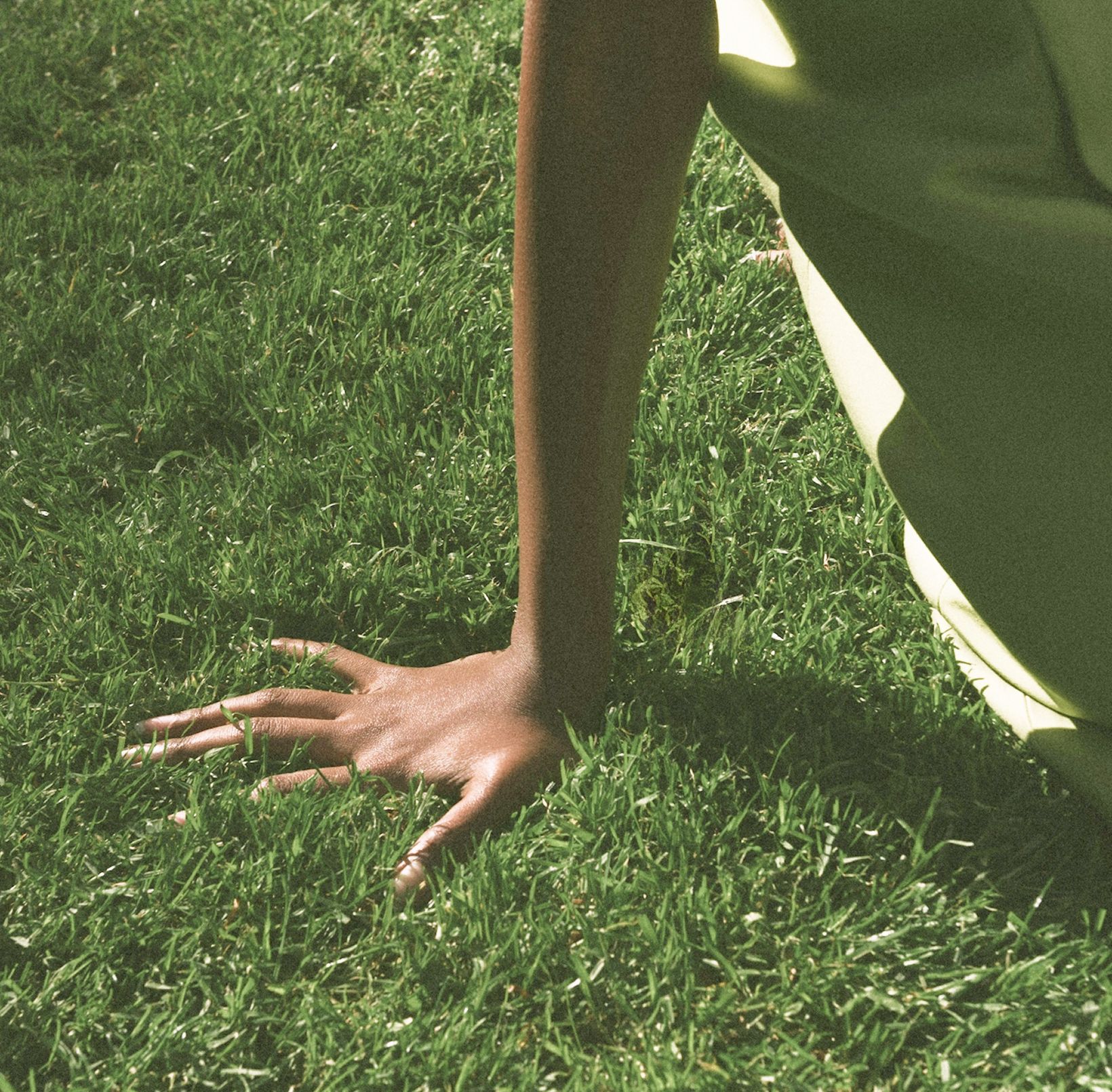 A hand resting palm-down on lush green grass with warm, sunlit vintage feel