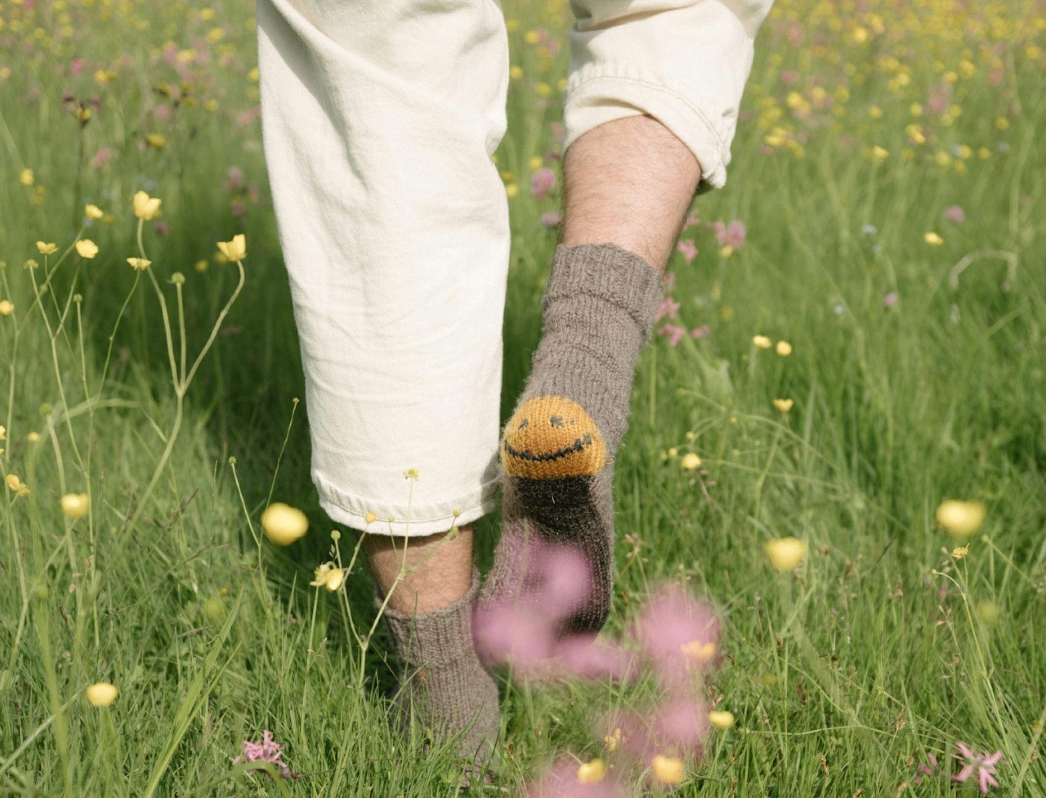 A person walking through a meadow wearing gray socks with a smiley face