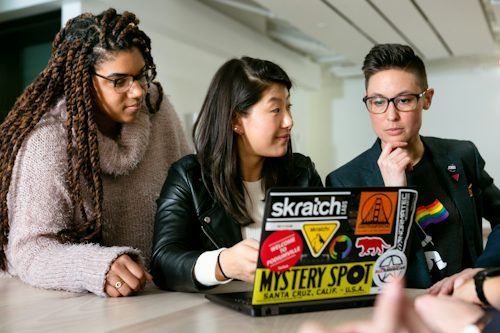 Three people collaborating around a laptop in a bright workspace