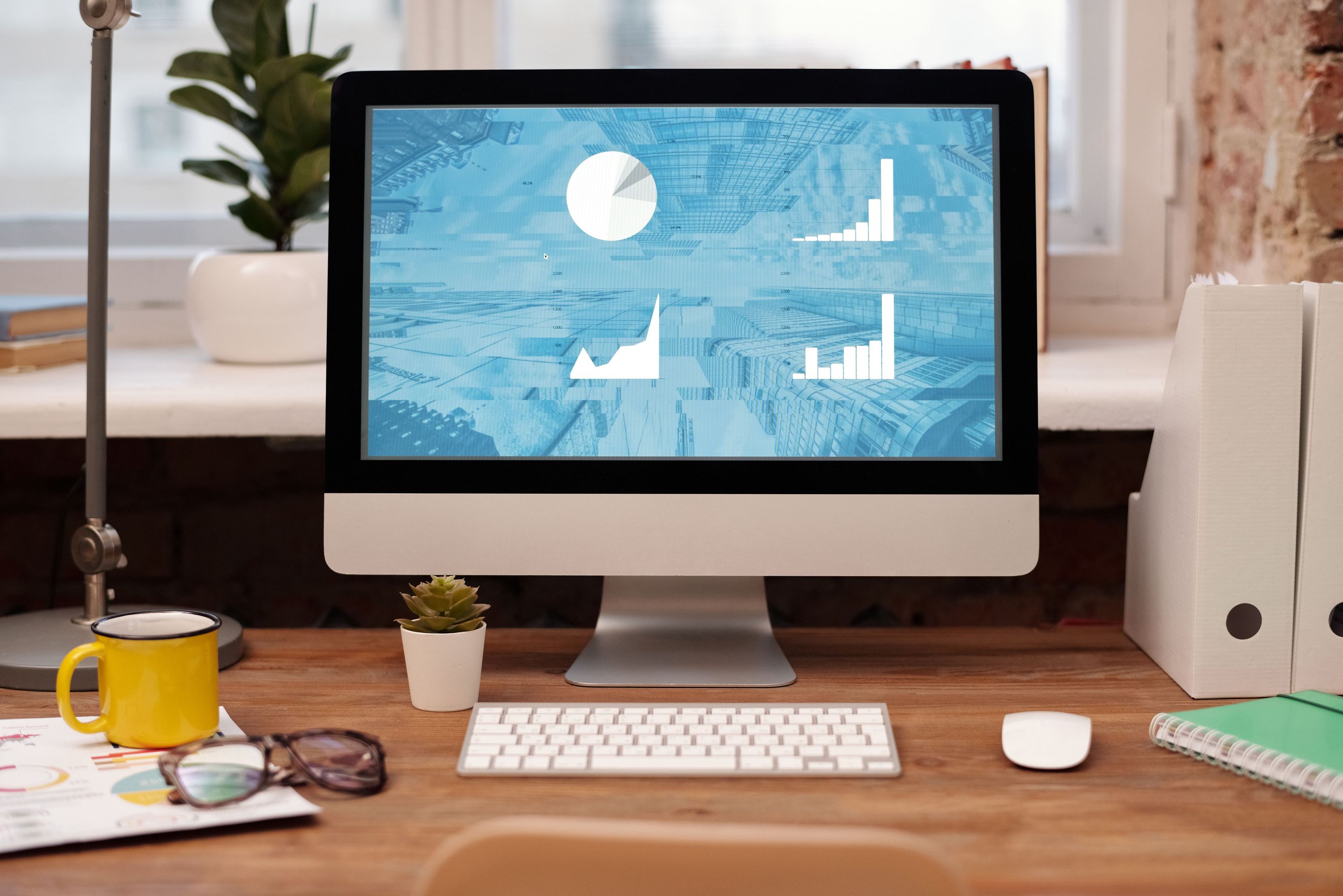 Desktop computer displaying charts on an organized desk with plants and a yellow mug