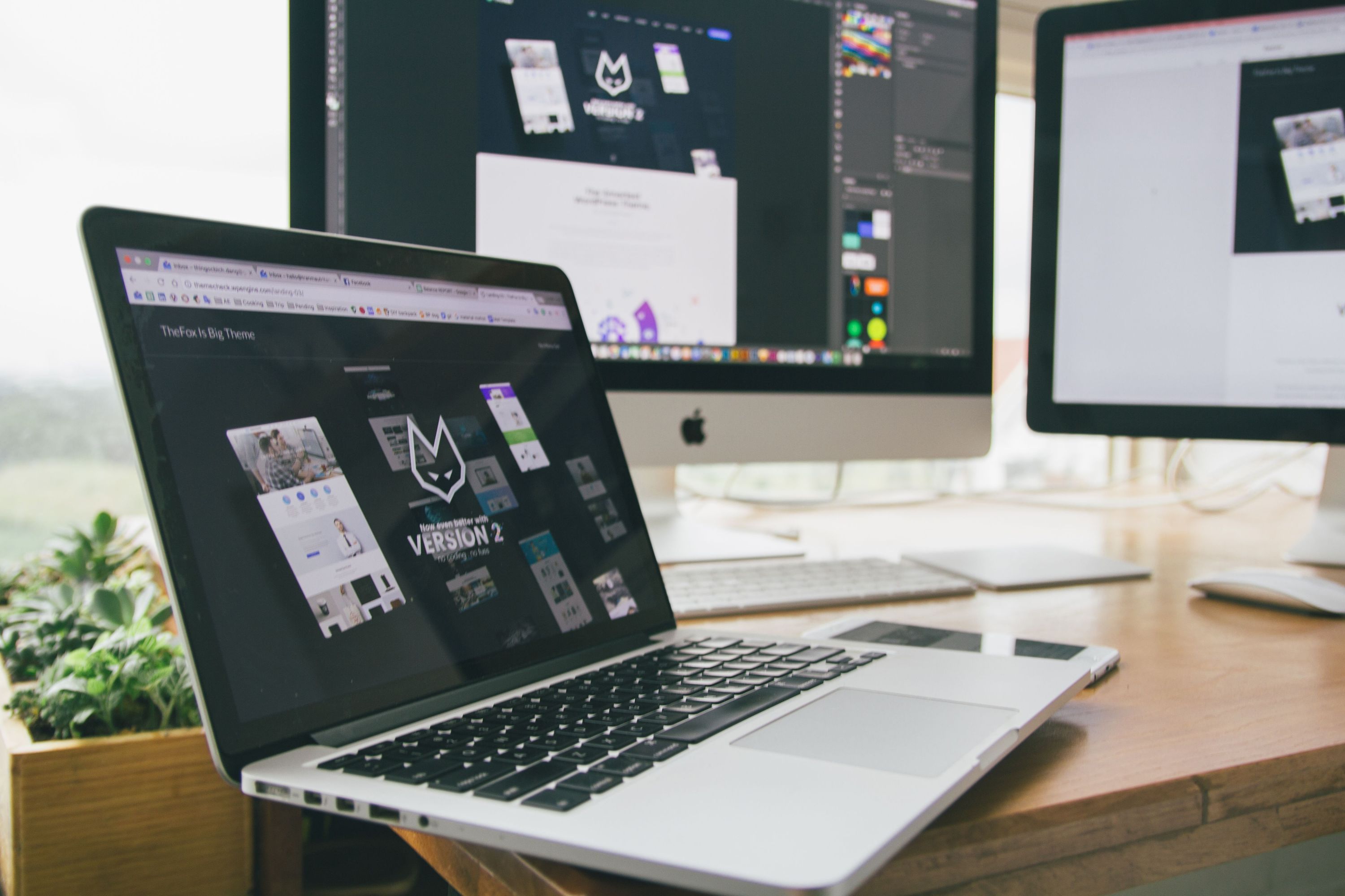 Web and graphic design layouts displayed across a laptop and two monitors