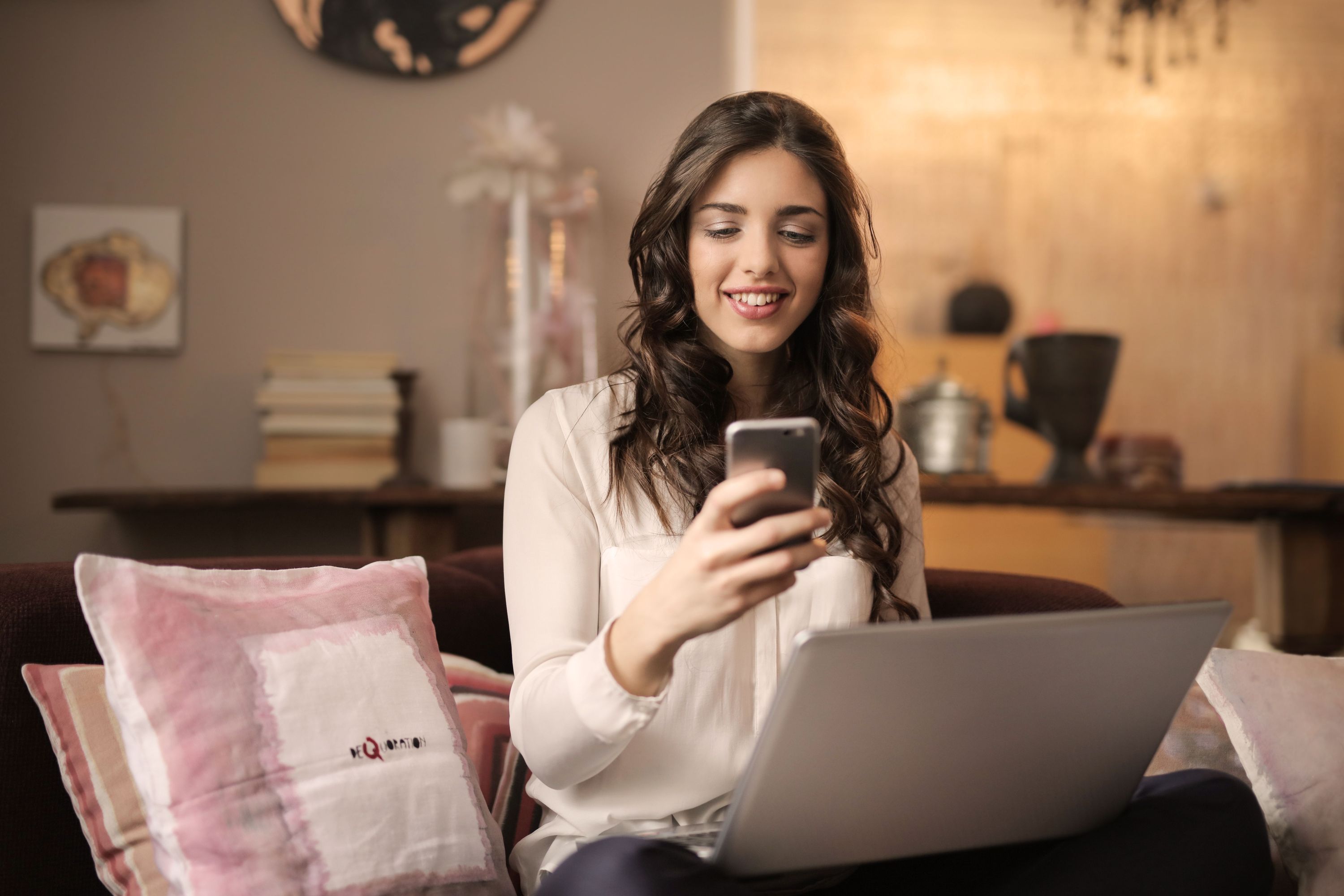 Woman using a smartphone beside an open laptop in a living room