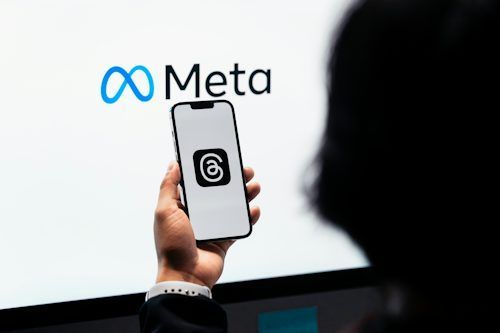 Person holding a smartphone displaying the Threads icon in front of the Meta logo