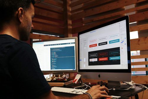 Person working at a desk with two monitors in a wood-paneled room