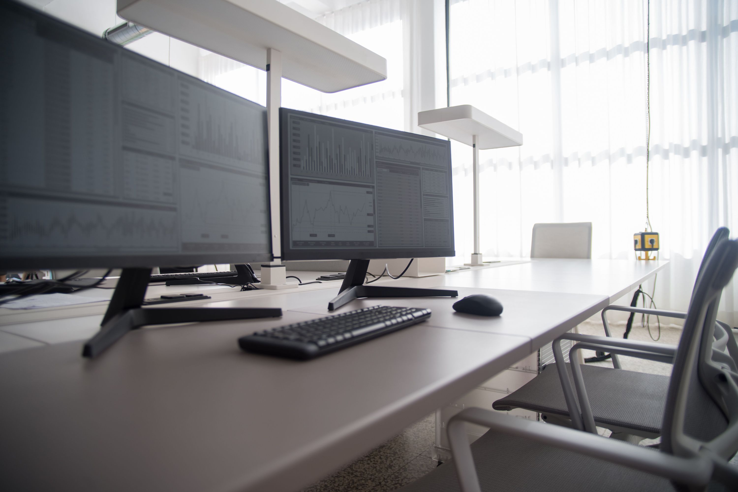 Office workstation with analytics dashboards on dual monitors beside large windows