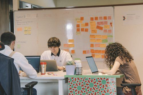 Team collaborating around a table in front of a whiteboard with colorful sticky notes