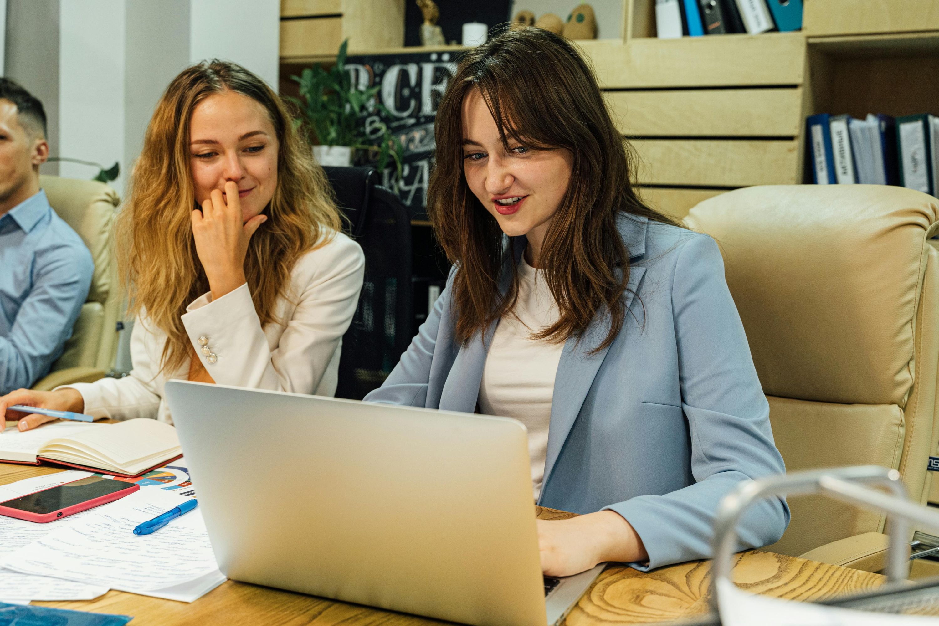 Two women working together on a laptop in a modern office setting