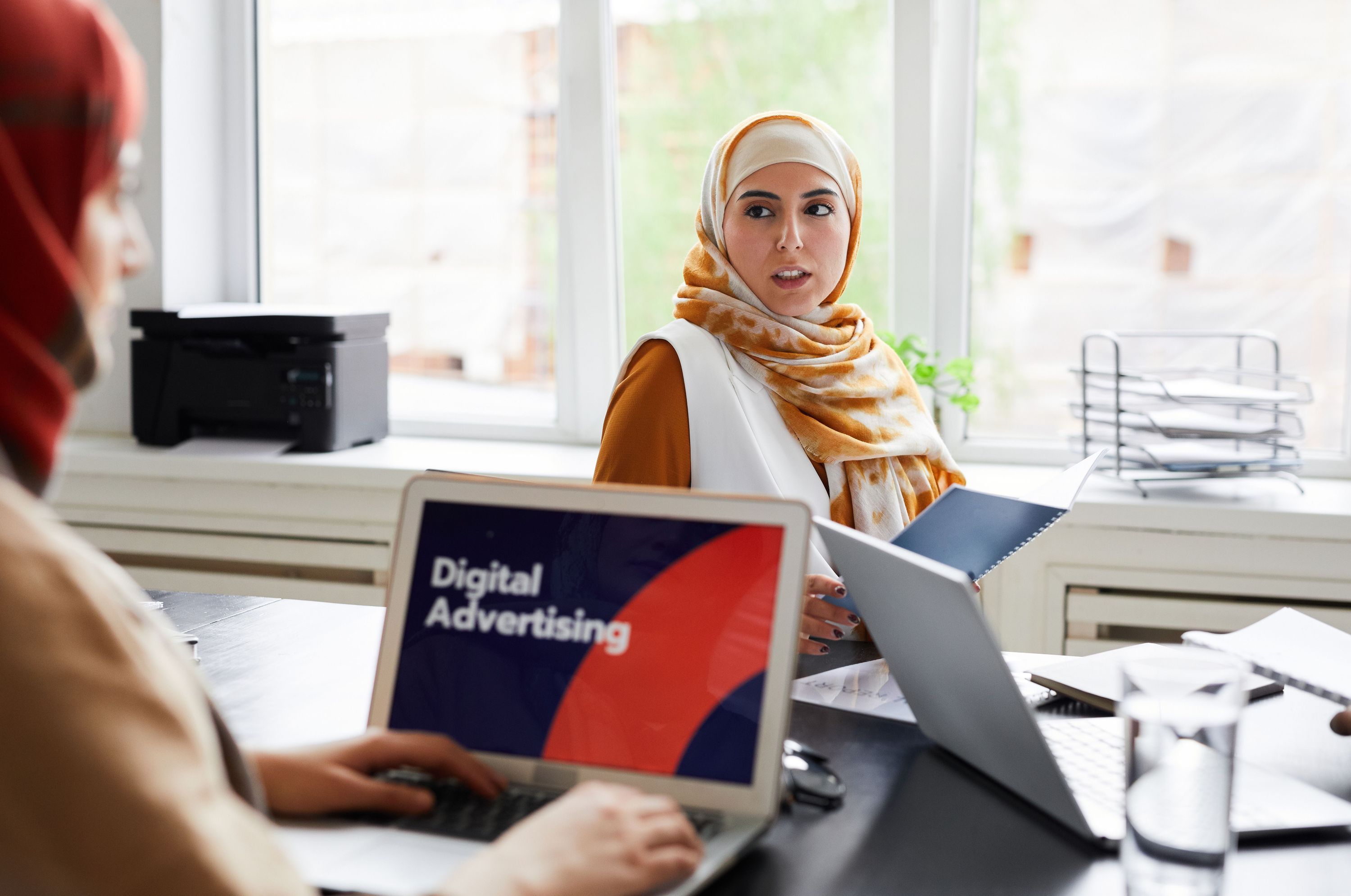 Colleagues discussing digital advertising at a desk with laptops in a bright office