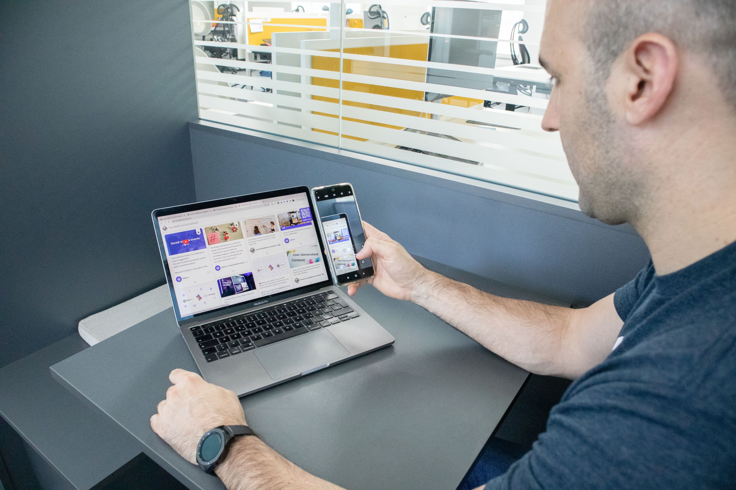 Marketer using a smartphone beside a laptop displaying a webpage