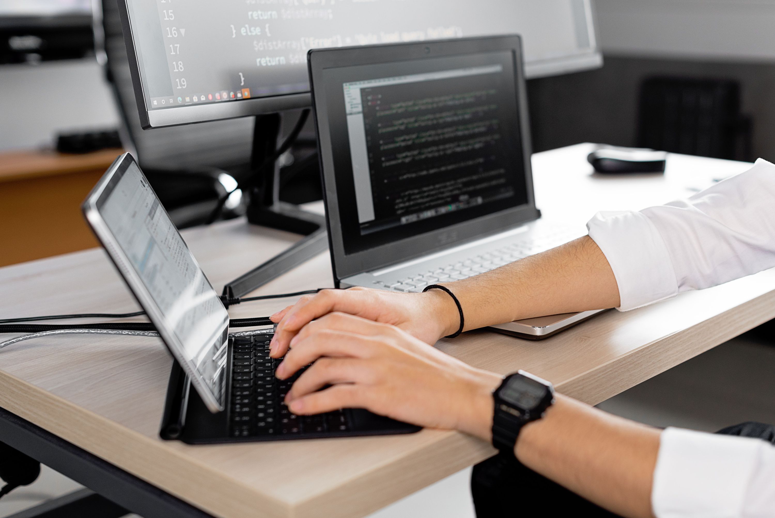 Developer working at a laptop with code displayed across multiple monitors