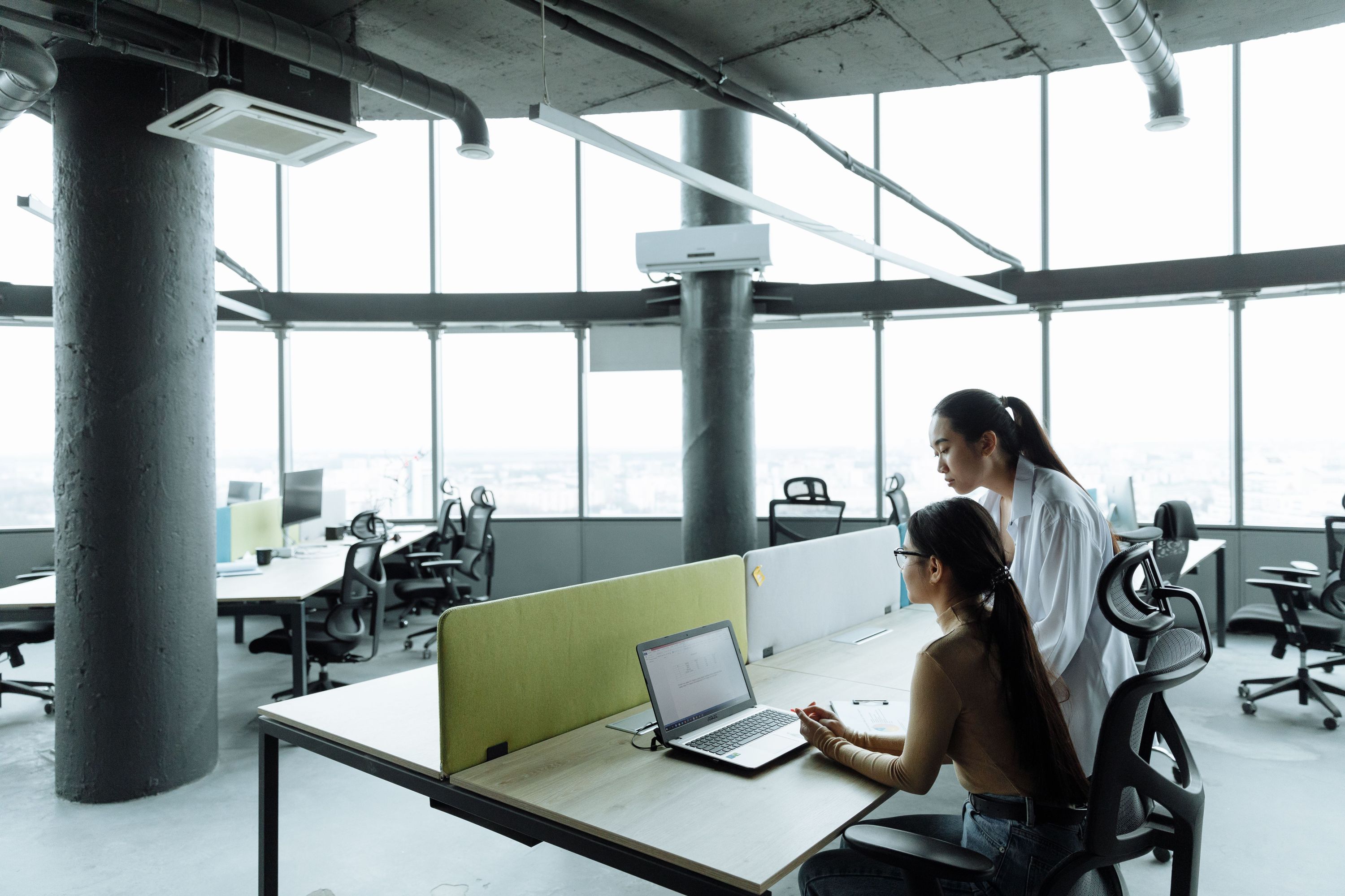 Two coworkers collaborating at a laptop in a bright, open-plan office
