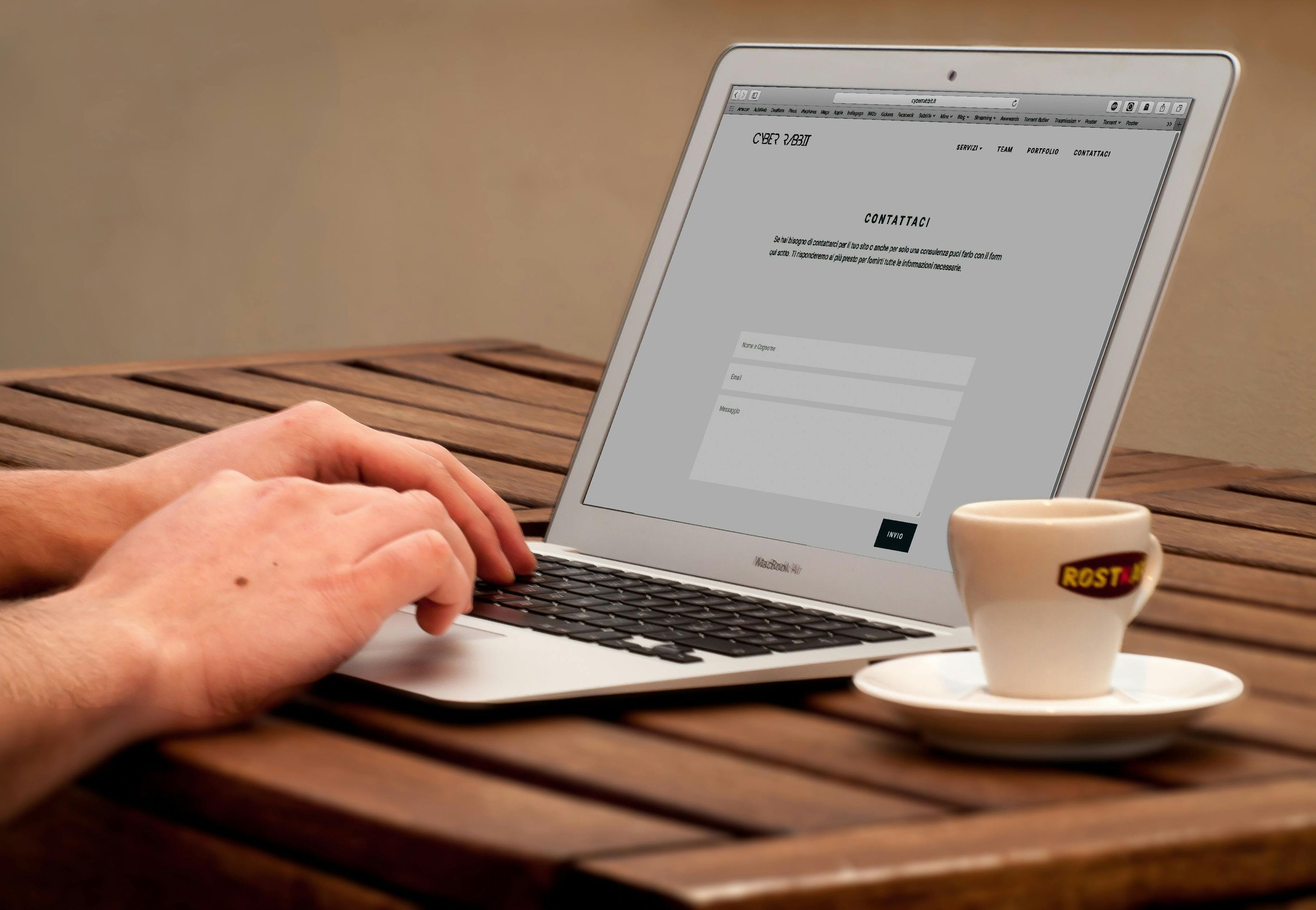 Person using a laptop beside a teacup on a wooden table